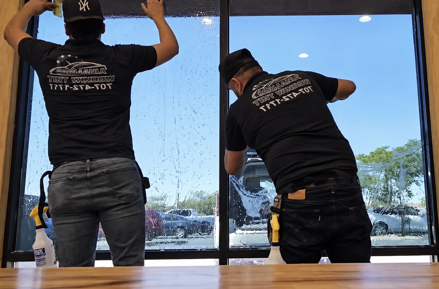 Two Armando Window Tint installers applying film to a storefront window